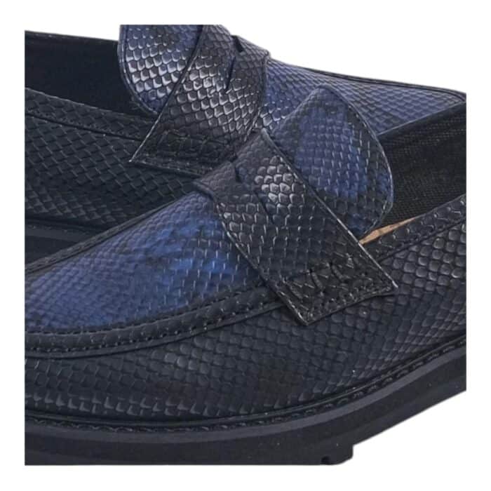 55 121 E | The Jonathan D Penny Moc Snake Eclipse in Black/Blue is a sophisticated yet contemporary loafer, designed with a high-quality PU upper that mimics the sleek appearance of genuine leather while ensuring durability and long-lasting wear. Featuring a striking black and blue color combination, this shoe seamlessly blends classic penny loafer elements—such as moccasin-style stitching and a contrast band across the vamp—with modern details like the iconic golden JONATHAN D branding at the back, making it an effortlessly stylish choice for both formal and casual occasions. With a cushioned footbed for superior comfort, a breathable interior lining to keep your feet cool, and a thick rubberized sole for excellent grip and support, this loafer not only elevates your style but also provides all-day comfort and stability for any setting.